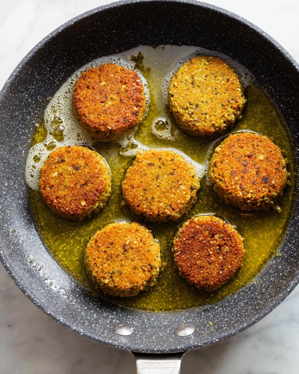 Seven round falafel patties with a textured, golden-brown crust fry in a dark speckled pan filled with bubbling yellow oil. The patties are evenly spaced in the pan, showing little bits of seeds and herbs in the crispy surface, giving a rough texture. The pan's handle is visible at the bottom, and it sits on a white marbled surface. photo taken with an iphone --ar 4:5 --v 7
