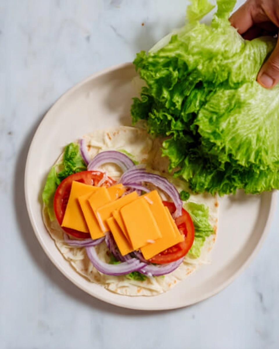 A white plate with one tortilla laid flat on a white marbled surface. The tortilla has a base layer of green lettuce leaves, topped with slices of red tomato. On top of the tomato slices, there are two layers of bright orange cheese squares. Thin rings of light purple onions are placed on top of the cheese. A woman's hand is holding fresh green leafy lettuce, positioned above the plate as if about to add more. The overall colors are fresh green, vibrant red, bright orange, and light purple against the soft white of the tortilla and plate. Photo taken with an iphone --ar 4:5 --v 7