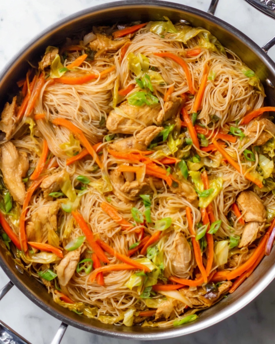 The image shows a large pan filled with a noodle dish. The base layer is thin white noodles with a slightly shiny texture. On top, there are pieces of light brown cooked chicken scattered across the noodles. Thin, bright orange carrot sticks and small green cabbage pieces are mixed evenly throughout. The colors are warm and natural, blending well with the light tones of the noodles. The pan sits on a white marbled surface. photo taken with an iphone --ar 4:5 --v 7