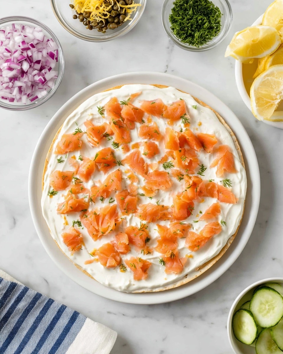 A round flatbread or tortilla is spread evenly with a thick layer of white cream cheese. Small, uneven chunks of orange smoked salmon are scattered over the cream cheese, creating a speckled pattern on top. The dish is placed on a white plate set on a white marbled surface. Around the plate, there are small clear bowls containing chopped red onions, green chopped herbs, capers, sliced cucumbers, and lemon zest, along with lemon wedges in a white bowl with a blue-striped cloth next to it. The overall look is fresh and colorful with the contrast between the creamy white base and the bright orange salmon pieces, all arranged neatly. photo taken with an iphone --ar 4:5 --v 7