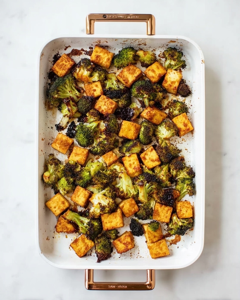 The image shows a white roasting pan with two bronze handles placed on a white marbled surface. Inside the pan, there are two layers of roasted food: the first layer consists of small broccoli florets that are green with some charred black and brown spots from roasting, scattered unevenly across the pan. The second layer consists of golden brown roasted tofu pieces, roughly square shaped, also sporadically spread throughout the pan. Some of the broccoli and tofu pieces have slightly crispy edges, showing texture and roasting marks. Photo taken with an iphone --ar 4:5 --v 7