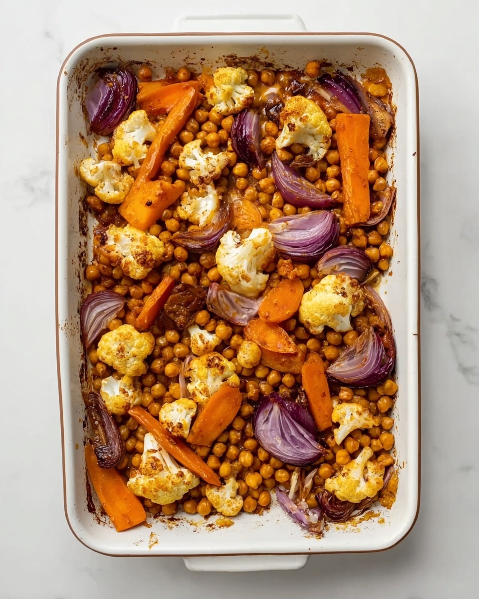 The image shows a white rectangular baking dish filled with roasted vegetables and chickpeas on a white marbled surface. The dish has a base layer of small, round, slightly browned chickpeas. On top, there are several bright orange carrot slices and large chunks of golden brown cauliflower. Scattered among the vegetables are pieces of red onion with deep purple and light red tones. The ingredients are spread evenly and the roasted texture is visible, showing slight charring and crisp edges. Photo taken with an iphone --ar 4:5 --v 7
