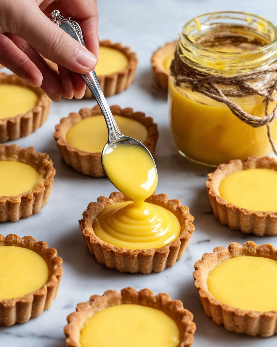 Small tart cases with a crisp golden-brown crust sit on a white marbled surface, each filled or being filled with a smooth, bright yellow creamy filling. A woman's hand holds a silver spoon above one tart, gently dropping the filling in its center, forming a soft mound. Nearby, an open glass jar wrapped with twine is filled with the same yellow filling. The scene shows multiple tarts at various stages: some empty crusts with scalloped edges and some fully filled with the glossy cream. photo taken with an iphone --ar 4:5 --v 7