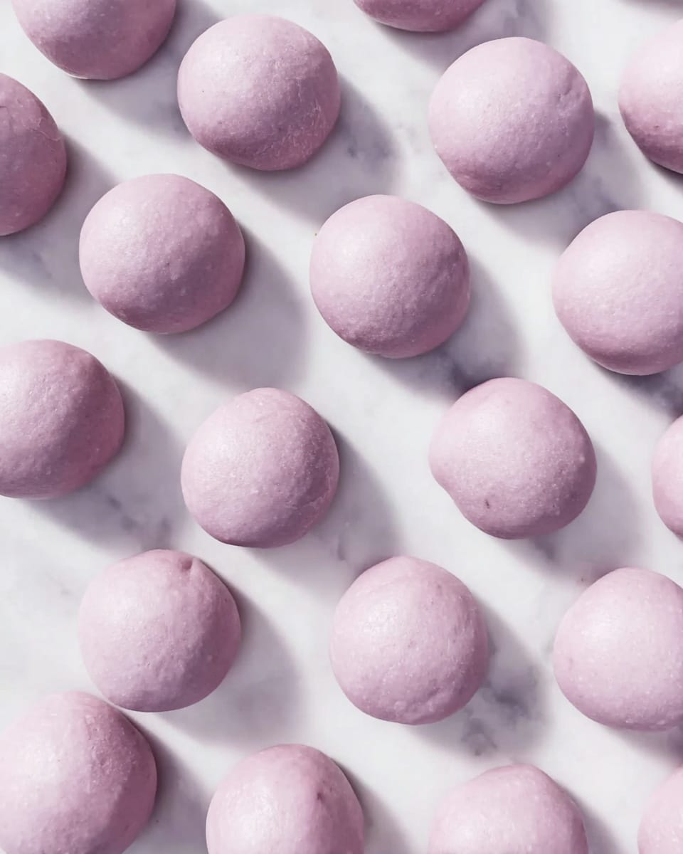 The image shows many small, round dough balls placed closely together on a white marbled surface. Each dough ball is smooth and has a pale purple color with a soft texture. They are evenly spaced and cover most of the surface in a scattered pattern. photo taken with an iphone --ar 4:5 --v 7