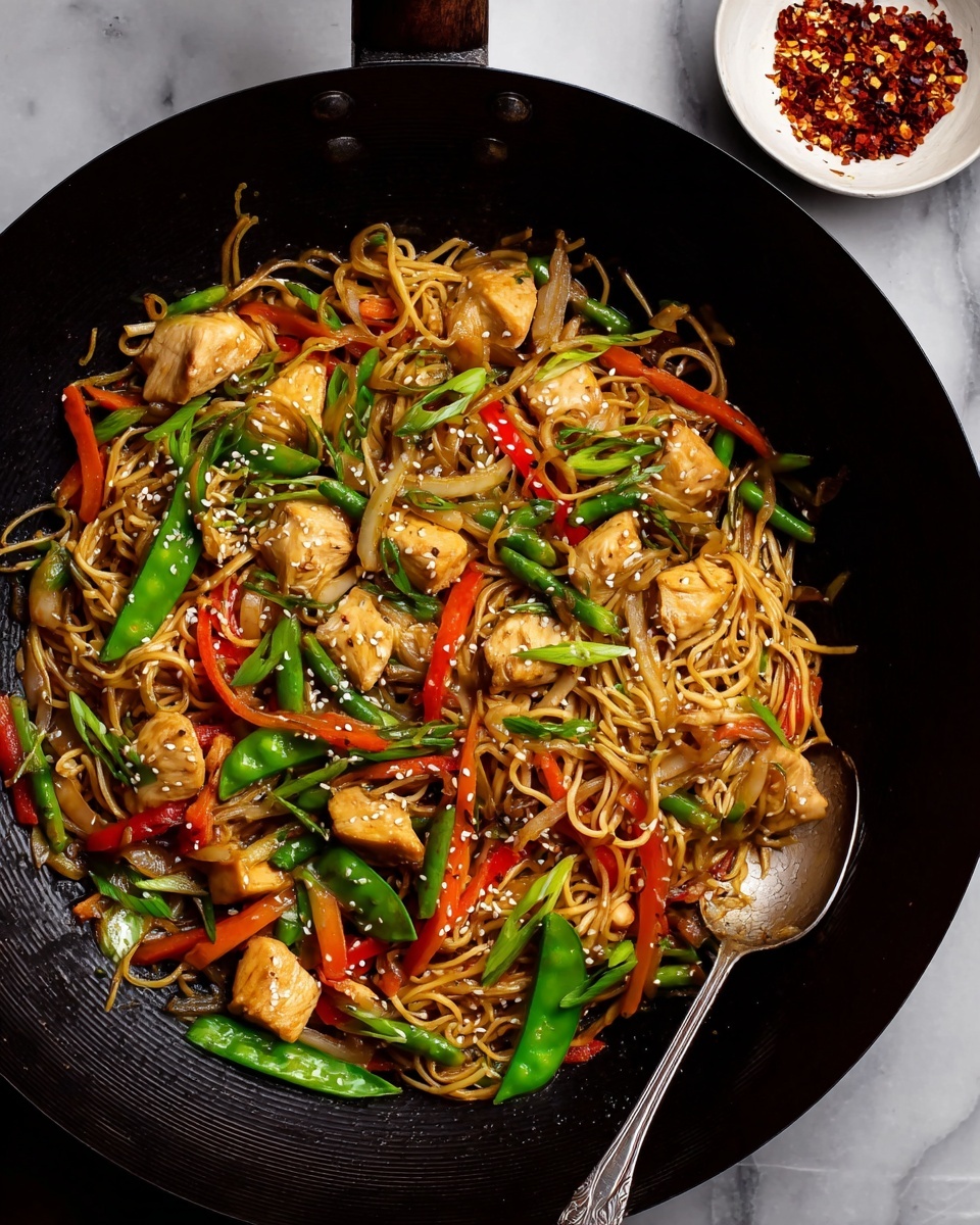 A large black wok holds a colorful stir-fry with three main layers: the base layer is light brown cooked noodles twisted around the dish; scattered evenly on top are chunks of light golden brown cooked chicken pieces; mixed throughout are bright green snap peas, long red bell pepper strips, orange carrot sticks, and translucent cooked onion slices. The stir-fry is garnished with small white sesame seeds and chopped green onions, adding texture and fresh green color. A metal spoon rests on the right side inside the wok, and in the upper right corner, a small white bowl holds crushed red pepper flakes. The background is a white marbled texture. photo taken with an iphone --ar 4:5 --v 7