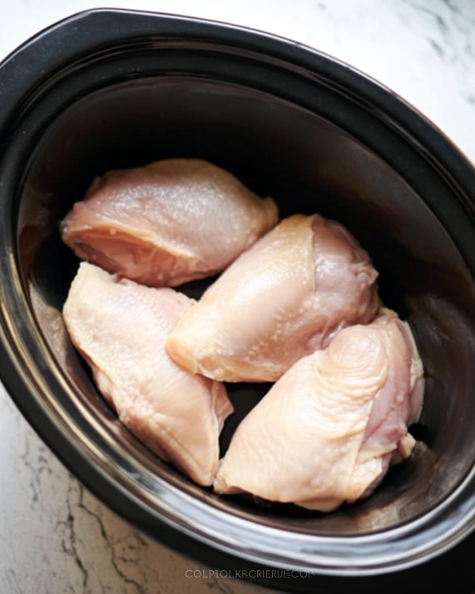 The image shows four raw chicken pieces placed in a black slow cooker. The chicken pieces are pale pink with a smooth and slightly shiny texture. They are arranged in a single layer, covering the bottom of the slow cooker evenly. The slow cooker has a rounded shape and a dark interior. The surface underneath shows a white marbled texture. Photo taken with an iphone --ar 4:5 --v 7