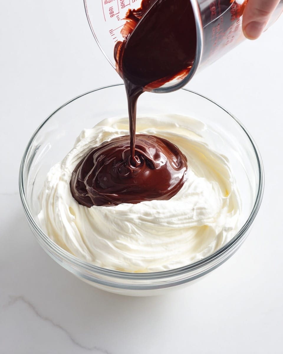 A glass bowl filled with whipped white cream has a rich dark brown chocolate sauce being poured into its center from a clear measuring cup held by a woman's hand. The contrast between the smooth, creamy white base and the glossy, thick chocolate creates a striking visual. The scene is set on a white marbled surface, highlighting the clean and fresh look of the ingredients. photo taken with an iphone --ar 4:5 --v 7