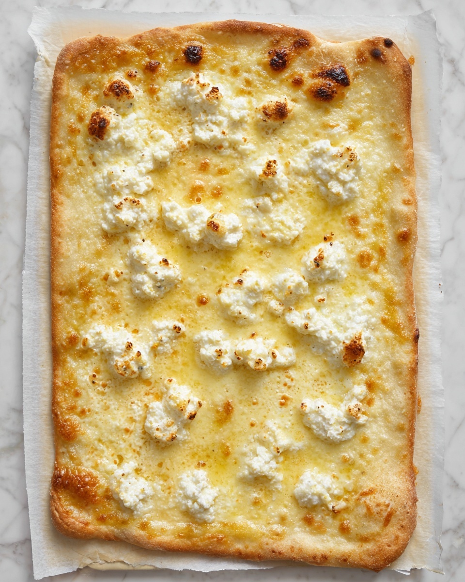 A rectangular pizza with a thin, golden-brown crust forms the base layer, slightly puffed and crispy around the edges. The next layer is a smooth, melted light-yellow cheese spread evenly across the surface, with some small browned spots showing slight bubbling. On top are scattered dollops of white, soft, creamy cheese, slightly charred on parts of their surface, giving a textured, uneven look. The entire pizza rests on white parchment paper, all placed on a white marbled surface. photo taken with an iphone --ar 4:5 --v 7