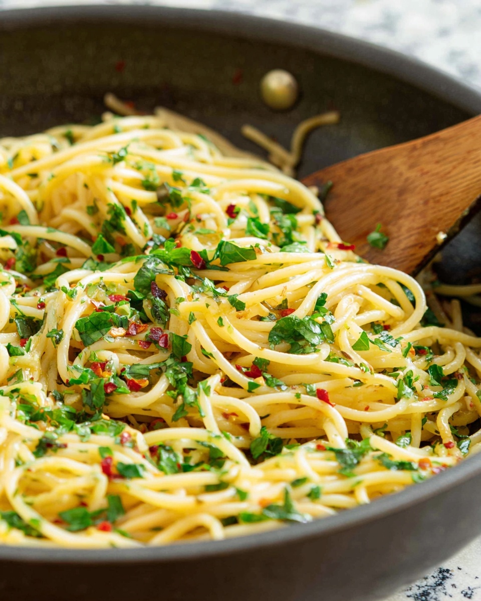 The image shows a close-up of cooked spaghetti pasta in a dark pan with a wooden spoon on the right side. The spaghetti is mixed with finely chopped green herbs scattered all over, adding bright green accents, and small red chili flakes sprinkled on top for a touch of color. The pasta looks soft and lightly shiny, with strands overlapping and curling naturally. The background features a white marbled texture, and the focus is on the front part of the pasta, making the details clear and vibrant. photo taken with an iphone --ar 4:5 --v 7