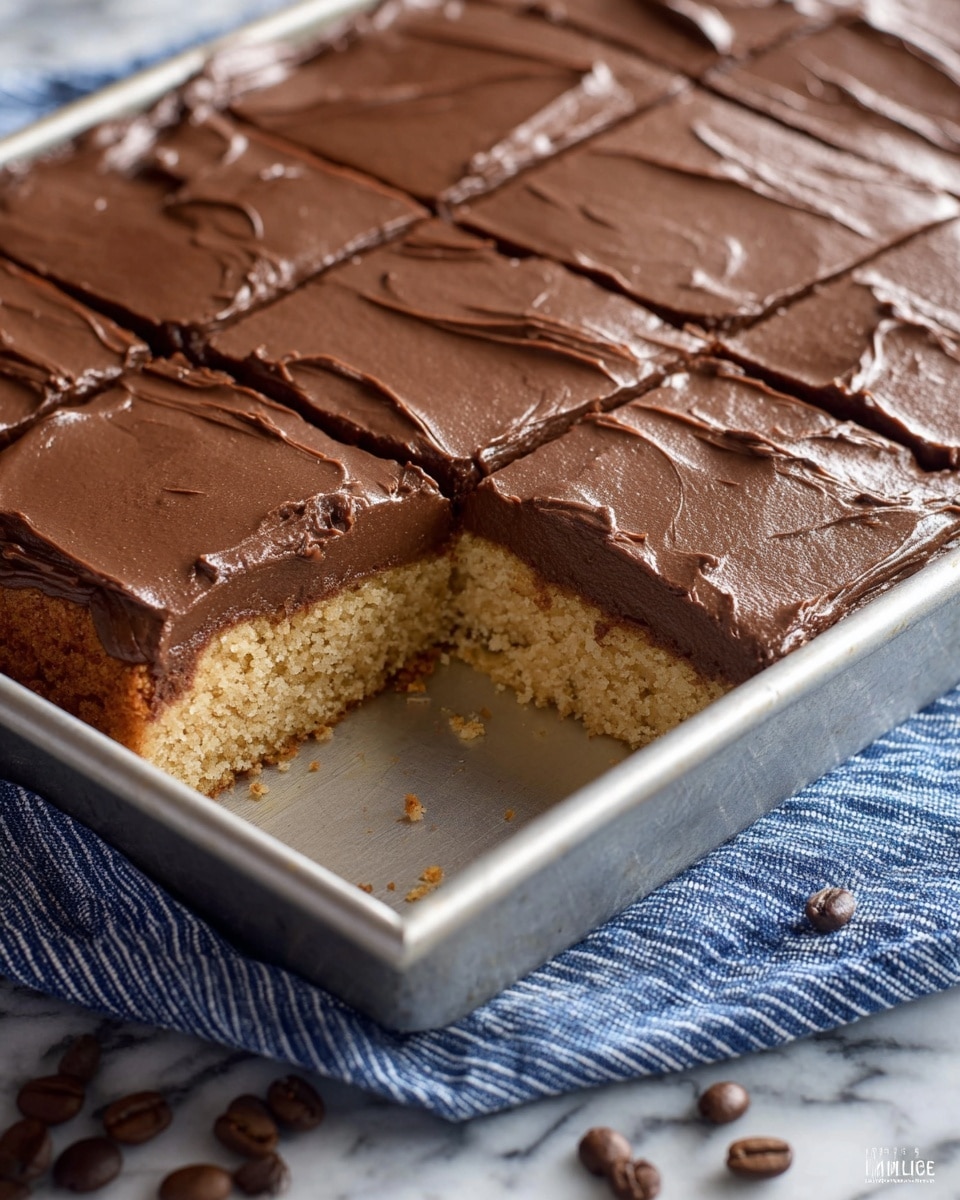 A rectangular cake in a silver baking pan is shown with two layers: the bottom layer is a light brown, soft, and crumbly cake, while the top layer is smooth chocolate frosting spread evenly across the whole surface. The cake is already cut into squares but one piece is missing from the corner, revealing the inside texture. The pan sits on a blue and white striped fabric with a few whole coffee beans scattered nearby. The background is a white marbled texture. Photo taken with an iphone --ar 4:5 --v 7