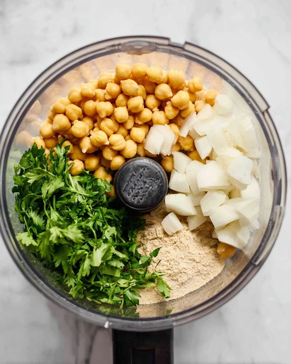 Inside a clear food processor bowl on a white marbled surface, there are four main layers: on the left side, golden yellow chickpeas fill nearly half the bowl; on the top right, uneven white chunks of onion sit; on the bottom right, a bunch of fresh green parsley leaves rests with stems; and below the chickpeas, a small amount of beige flour or ground spice is visible. The black center part of the food processor is visible in the middle, dividing the ingredients. Photo taken with an iphone --ar 4:5 --v 7