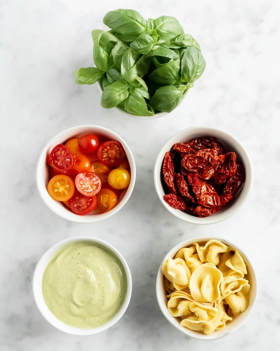 The image shows five small white bowls arranged on a white marbled surface. The top bowl has fresh green basil leaves with a smooth texture. Below it to the left, there is a bowl filled with small red and orange cherry tomatoes, some whole and some sliced, showing a juicy interior. To the right of the tomatoes, there is a bowl of dried red sun-dried tomatoes with a wrinkled and dense texture. Below the tomatoes bowl on the left, there is a bowl with a light green creamy sauce, smooth and thick. To the right of the sauce bowl is a bowl containing pale yellow tortellini pasta, folded and layered closely together. Photo taken with an iphone --ar 4:5 --v 7