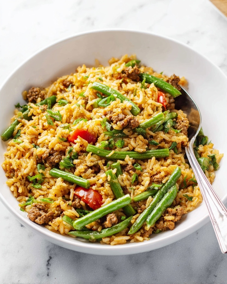 A white bowl is filled with a mix of fluffy yellow-brown rice, small pieces of cooked ground meat, bright green green beans cut into short pieces, and scattered bits of red tomato. A silver spoon is partially inside the bowl on the right side. The bowl sits on a white marbled surface, adding a clean and fresh look to the scene. The textures of the rice, meat, and green beans vary, with the rice soft and grains separate, the meat crumbly, and the green beans smooth and firm. photo taken with an iphone --ar 4:5 --v 7