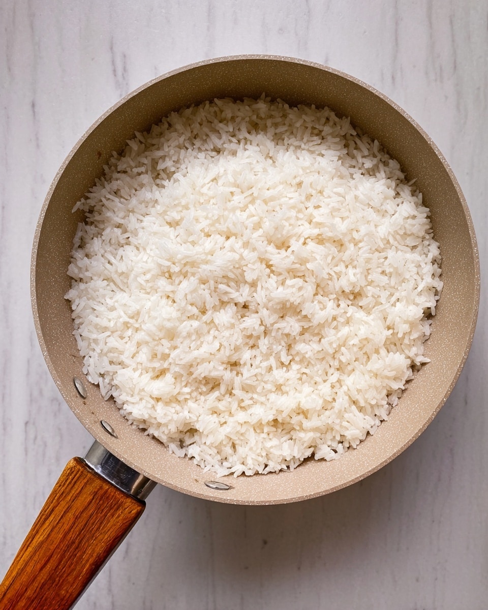 A single layer of cooked white rice fills the inside of a round beige pan with a wooden handle, the rice has a fluffy and soft texture, and the pan sits on a white marbled surface. photo taken with an iphone --ar 4:5 --v 7