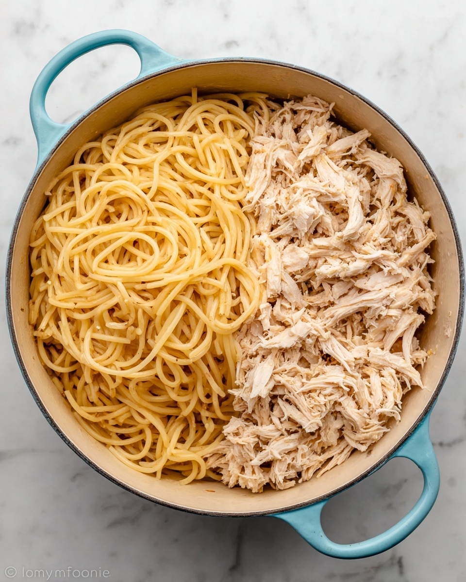 A large round pot with light blue handles sits on a white marbled surface. Inside, the pot is filled with two layers: on the left half, there is a thick layer of cooked spaghetti noodles in a pale yellow color, and on the right half, a layer of shredded light beige chicken. The noodles have a slightly shiny texture, and the shredded chicken looks soft with visible small chunks and strands. Photo taken with an iphone --ar 4:5 --v 7