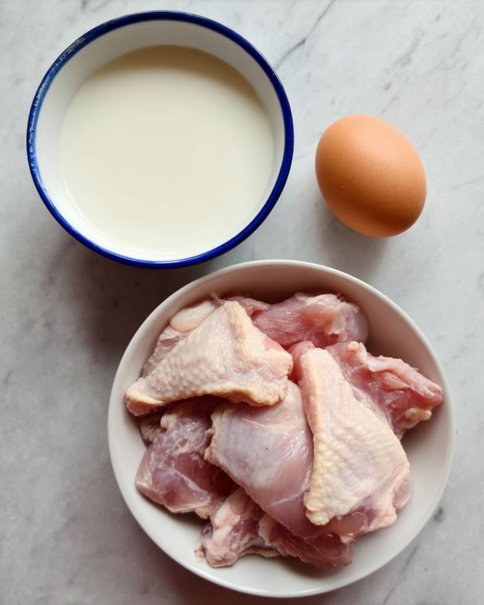 The image shows three main items placed on a white marbled surface. At the top left, there is a white bowl with a blue rim filled with a white liquid. To the right of the bowl, there is a single brown egg. Below these items, a white bowl contains several raw pieces of chicken with light pink skin and some texture visible on the surface. The chicken pieces fill most of the bowl, and the arrangement looks neat and fresh. photo taken with an iphone --ar 4:5 --v 7