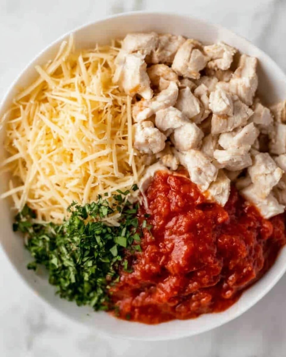 A white bowl on a white marbled surface holds four separate sections of ingredients. One section has shredded pale yellow cheese with a soft texture. Next to it is a pile of small, light beige cooked chicken pieces with a chewy look. Another section shows bright green chopped herbs with a fresh, leafy texture. The last section contains a thick, bright red tomato sauce with a smooth, slightly chunky texture. Photo taken with an iphone --ar 4:5 --v 7