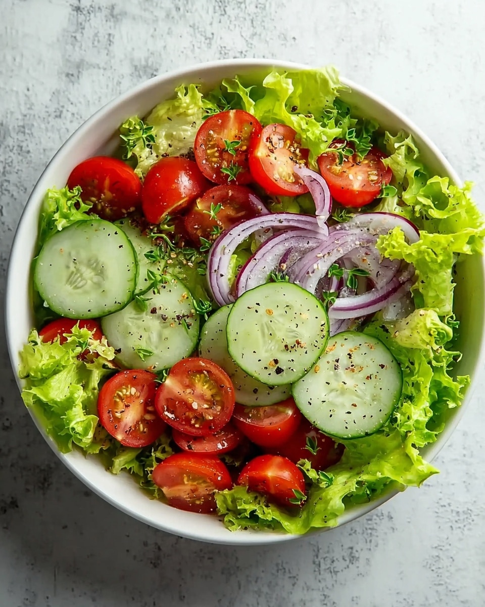 A fresh salad in a white bowl with three layers: the bottom layer is bright green leafy lettuce with ruffled edges, the middle layer consists of thinly sliced cucumber rounds with a pale green center and darker green skin, and the top layer includes halved cherry tomatoes that are bright red with a juicy texture, and thin slices of red onion with white and purple rings. The salad is sprinkled lightly with coarse black pepper and small green herb leaves. The bowl sits on a white marbled surface. photo taken with an iphone --ar 4:5 --v 7