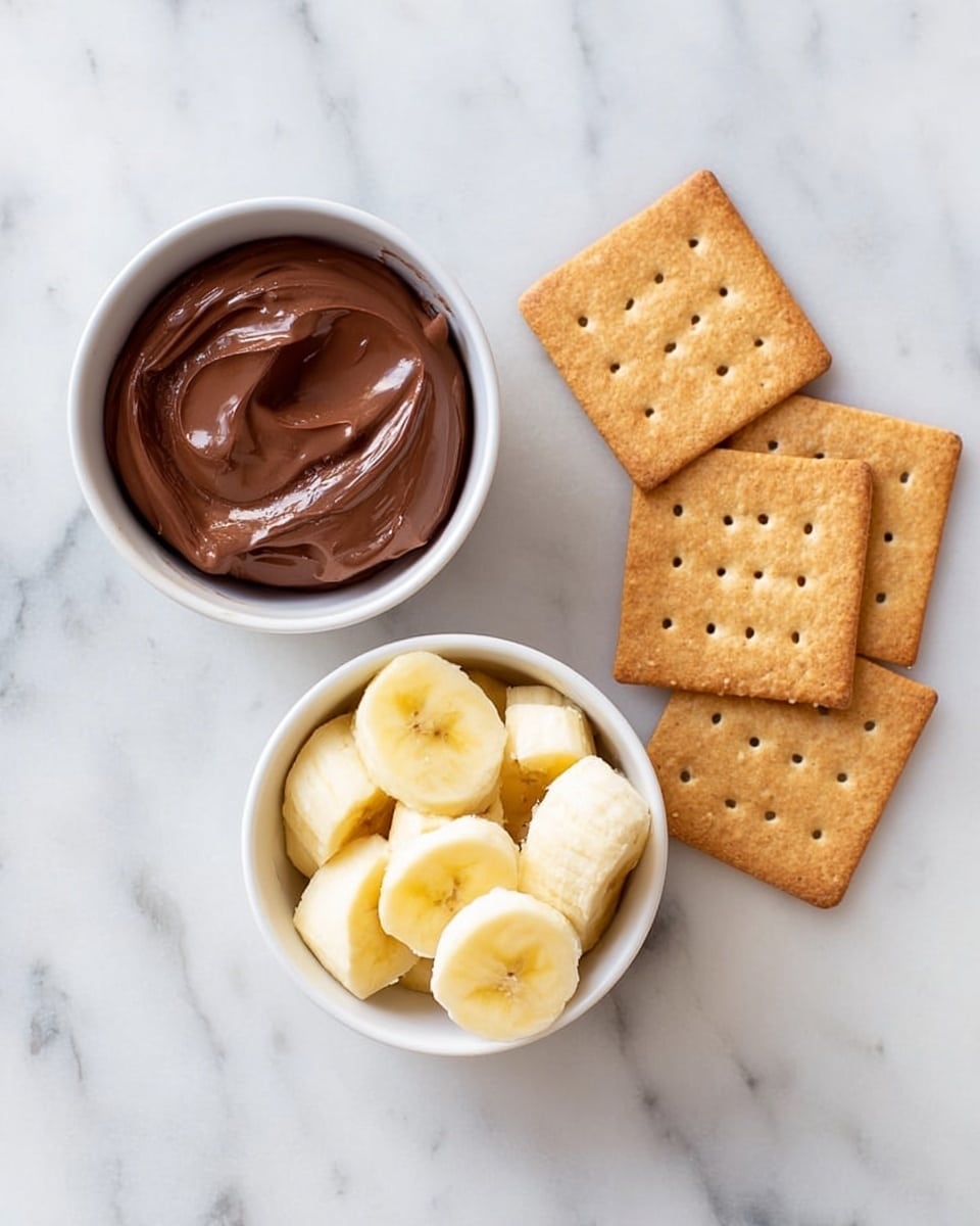The image shows a white marbled surface with two small white bowls and five whole wheat square crackers. One bowl is filled with smooth chocolate spread, dark brown in color with a creamy texture. The other bowl contains sliced banana pieces, light yellow with a soft texture. The five crackers are arranged loosely to the right of the bowls, each golden brown with small holes on the surface. photo taken with an iphone --ar 4:5 --v 7