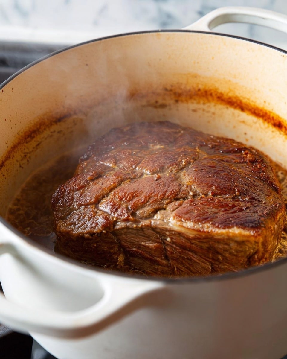 A large piece of browned meat with a deep golden crust is inside a white pot, showing a rich texture with small bubbles of fat and juices around it. The meat is thick and covers most of the pot with light steam rising above it, giving a hot and fresh look. The pot has white handles visible on both sides, resting on a stove, with the inside showing some browning residue on the sides. The background is a white marbled texture. photo taken with an iphone --ar 4:5 --v 7