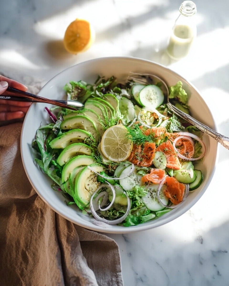 The image shows a white bowl filled with a fresh green salad placed on a white marbled surface. The salad has several layers: the bottom layer is a mix of leafy greens, topped with thin slices of avocado arranged in a fan shape on one side. There are also bright orange pieces of cooked fish scattered around, along with thin, translucent rings of white onion spread evenly. A few cucumber slices and sprigs of herbs add more green details. Half a lemon with a bright yellow color sits on the side inside the bowl. A pair of silver utensils rests on the edge of the bowl. A small clear bottle of dressing or sauce is in the background. A woman's hand is reaching with chopsticks inside the bowl. The scene is lit with natural light, giving a fresh and healthy feel photo taken with an iphone --ar 4:5 --v 7