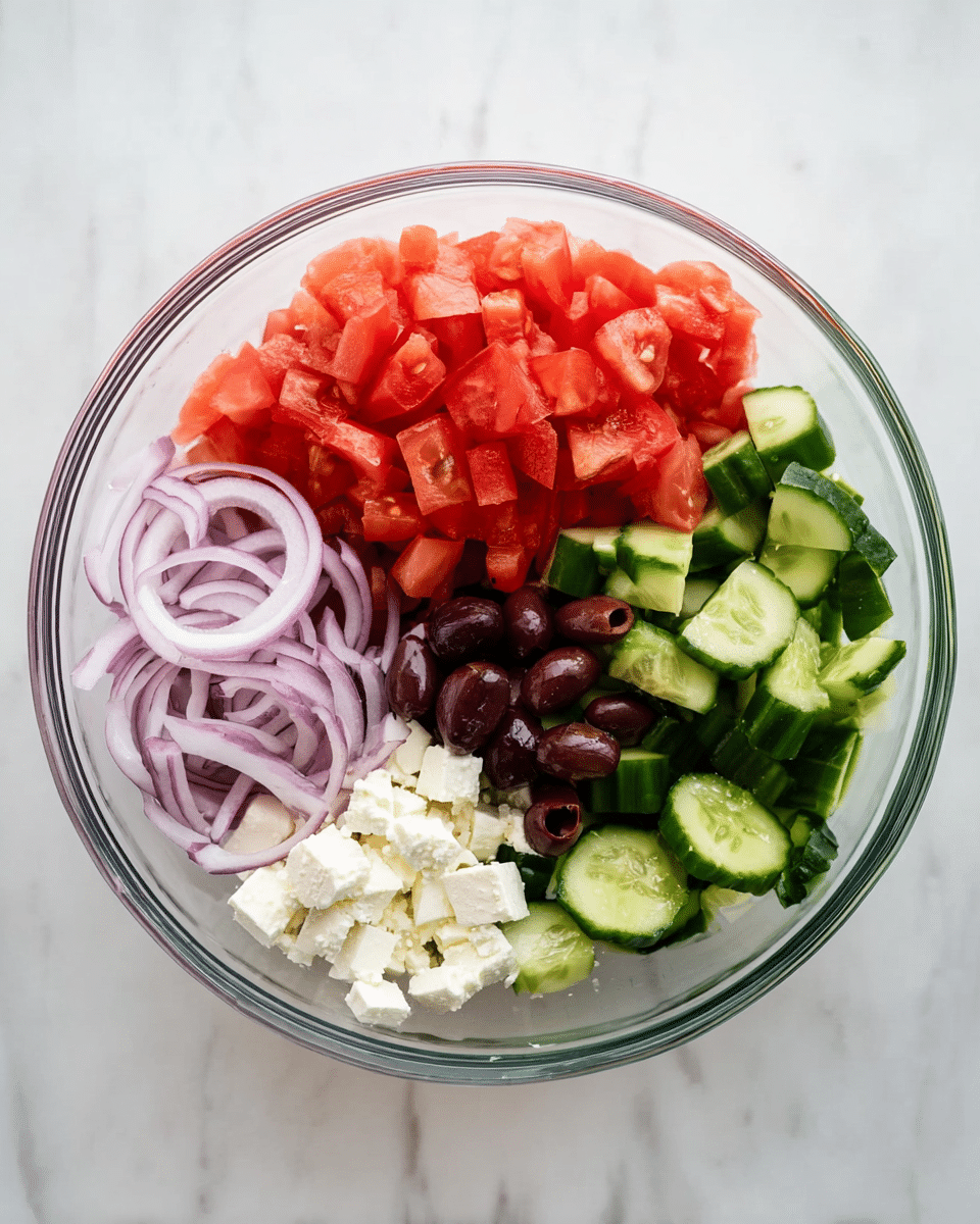 A clear glass bowl on a white marbled surface contains five separate layers of fresh salad ingredients. On the top right, there are bright red, chopped tomato pieces with a soft texture. Next to the tomatoes on the right, thick slices of green cucumber with a dark green skin and pale green inside are placed. Below the cucumber, there is a small pile of white, chunky feta cheese. To the left of the cheese, a group of sliced dark purple olives adds contrast. On the far left, thin strips of light purple onion complete the salad. The ingredients are neatly arranged and not mixed, showing each element clearly. Photo taken with an iphone --ar 4:5 --v 7