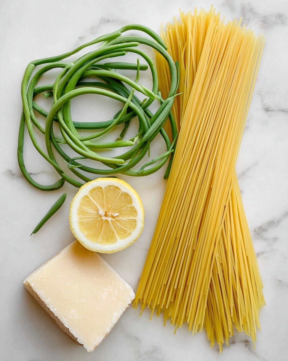 The image shows three main items neatly placed on a white marbled surface: on the right side, there is a bundle of uncooked thin yellow pasta stacked in a straight line; on the left side at the top and middle, there are two twisted loops of long green garlic scapes with a fresh texture; between the two loops of scapes, there is a half lemon with visible juicy segments facing upwards; at the bottom left corner, there is a chunk of pale, hard cheese with a slightly rough texture. photo taken with an iphone --ar 4:5 --v 7