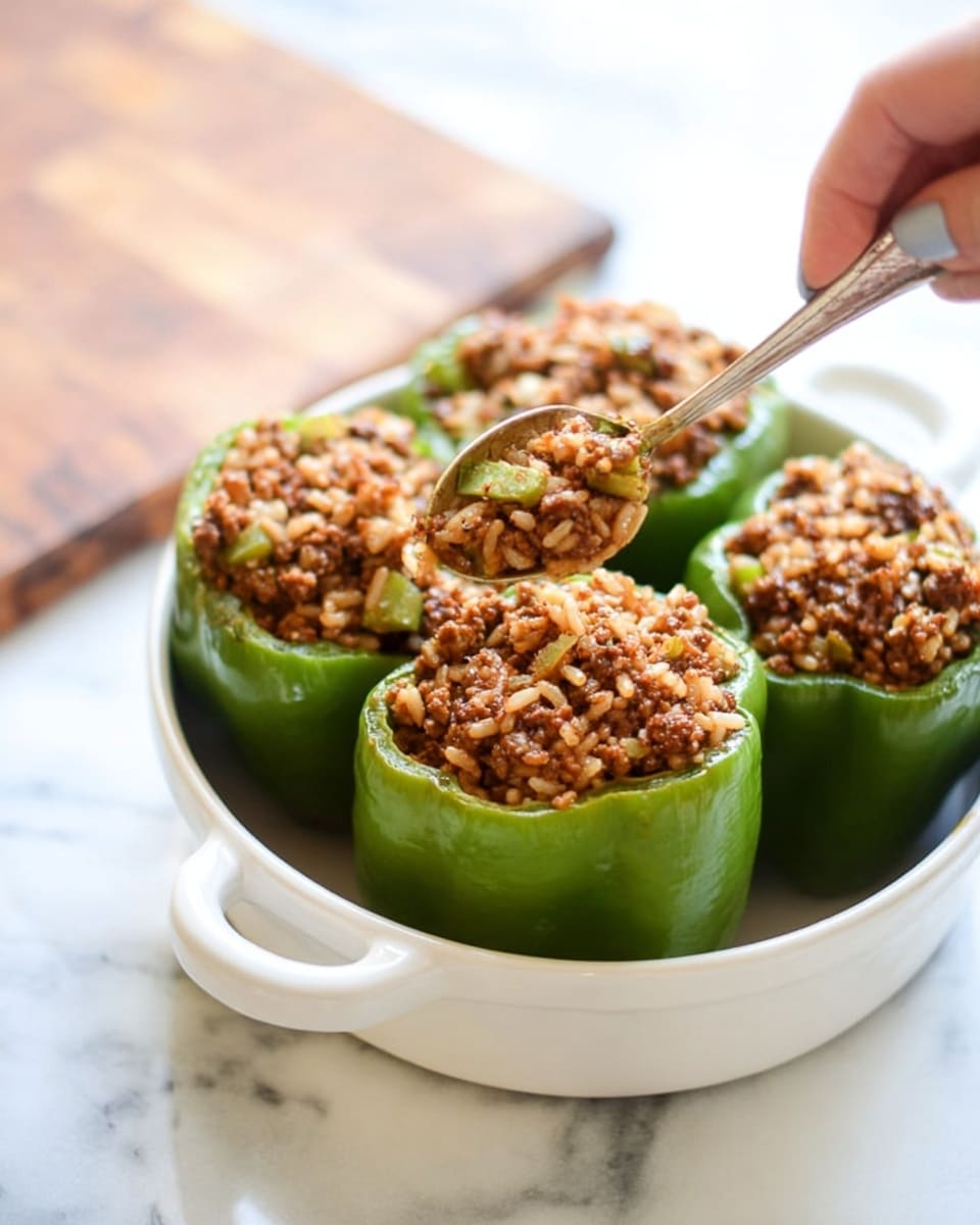 Four green bell peppers stand upright in a white bowl with handles, each filled to the top with a textured mixture of cooked ground meat, rice, and small bits of vegetables. The mixture is a rich brown color with visible white and green pieces. A woman's hand holds a spoon above one pepper, gently adding more of the savory filling. The bowl sits on a white marbled surface, with a wooden cutting board slightly blurred in the background, enhancing the fresh kitchen feel. Photo taken with an iphone --ar 4:5 --v 7