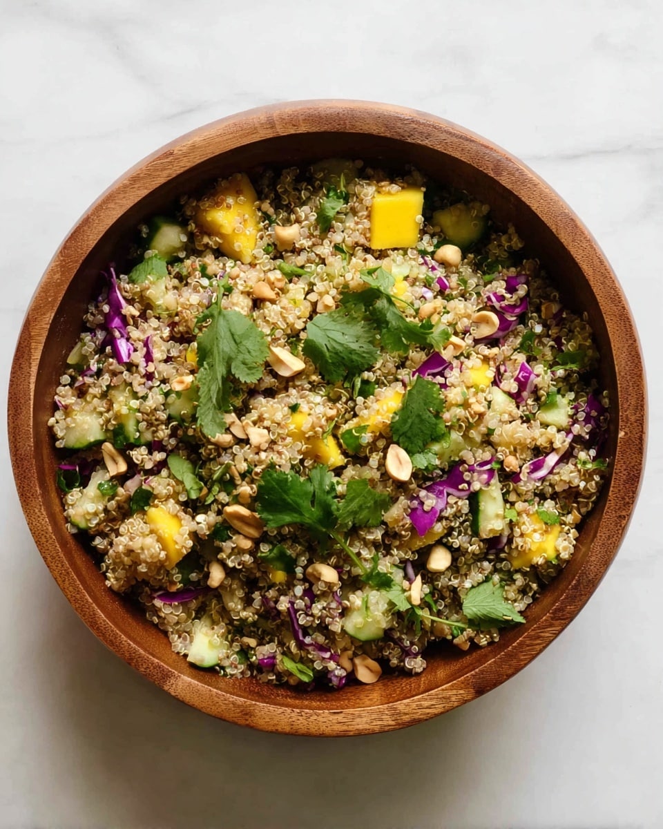 A wooden bowl filled with a quinoa salad showing a mix of small, light beige quinoa grains as the main layer, scattered with bright yellow mango chunks, small pieces of green cucumber, thin strips of purple cabbage, and light brown peanuts. There are fresh green cilantro leaves spread on top. The bowl is placed on a white marbled surface. photo taken with an iphone --ar 4:5 --v 7