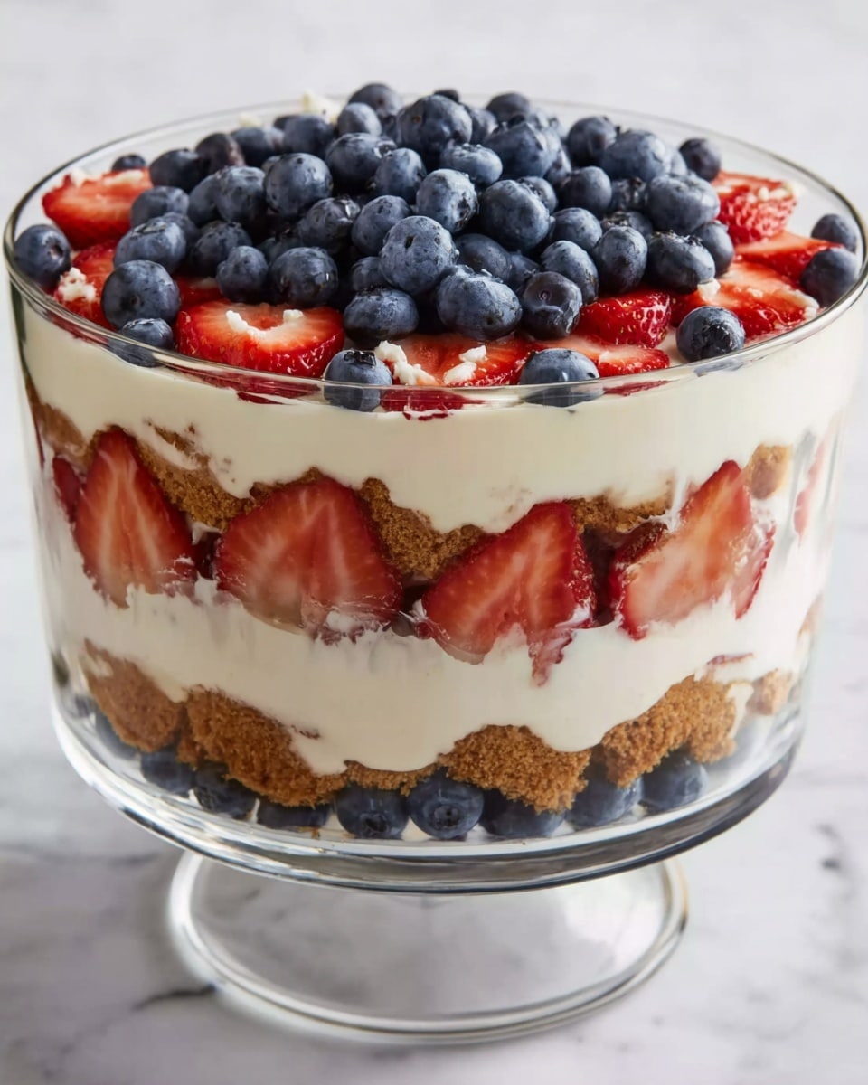 A clear glass trifle bowl shows multiple layers of dessert. The bottom layer is crumbly light brown crust. Above it is a thick creamy white layer. Next is a layer with fresh sliced strawberries arranged around the bowl’s inside, with more creamy white filling in the middle. Another crumbly light brown layer follows. Then, more creamy white filling with strawberry slices inside it. The topmost layer is a dense pile of fresh blueberries covering the entire surface. The bowl is placed on a white marbled surface. Photo taken with an iphone --ar 4:5 --v 7