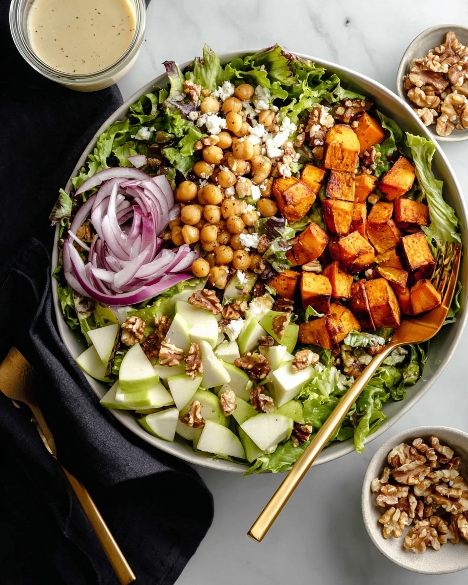 A white bowl filled with a colorful salad sits on a white marbled surface. The base layer is green leafy lettuce, topped with roasted orange sweet potato cubes arranged to one side. Scattered on top are beige chickpeas, light green apple cubes, thin red onion slices, and brown walnut pieces. A small amount of white cheese is dotted around the salad. A large golden spoon and fork rest inside the bowl on the right side. Nearby, small white bowls hold extra walnuts and white onion slices, with a clear glass of creamy dressing close by. Photo taken with an iphone --ar 4:5 --v 7