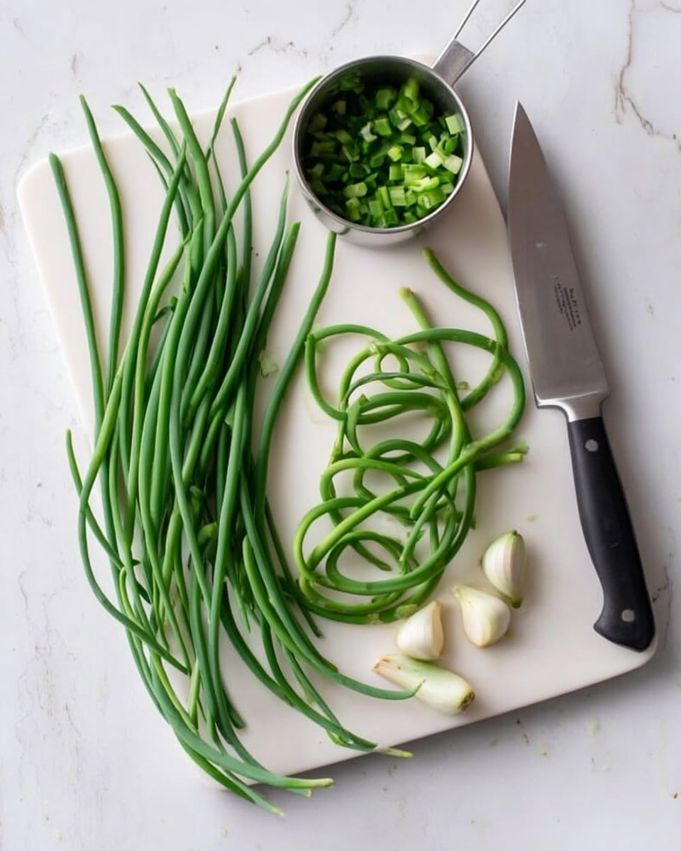 The image shows a white cutting board on a white marbled surface with fresh green garlic scapes arranged in three groups: long uncurled scapes on the left, several curved scapes in the middle, and a few whole green onions with bulbs on the right. A small metal measuring cup filled with chopped garlic scapes sits near the top middle of the board. Next to the green onions on the right side of the cutting board is a large knife with a black handle and a shiny blade. The scene is well-lit and clean with a simple layout, photo taken with an iphone --ar 4:5 --v 7