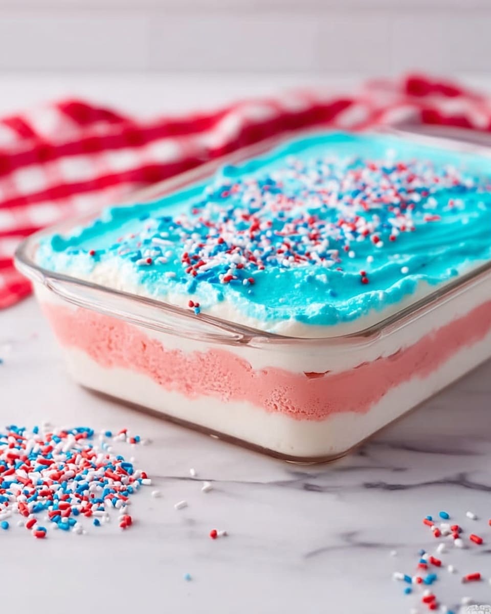 The image shows a clear glass rectangular dish with three visible layers of dessert. The bottom layer is light pink with a smooth texture, the middle layer is white and creamy, and the top layer is bright blue with a smooth texture, sprinkled with small red, white, and blue sprinkles. The dish is placed on a white marbled surface with a red and white checkered cloth to the left, and some sprinkles scattered around the dish. Photo taken with an iphone --ar 4:5 --v 7