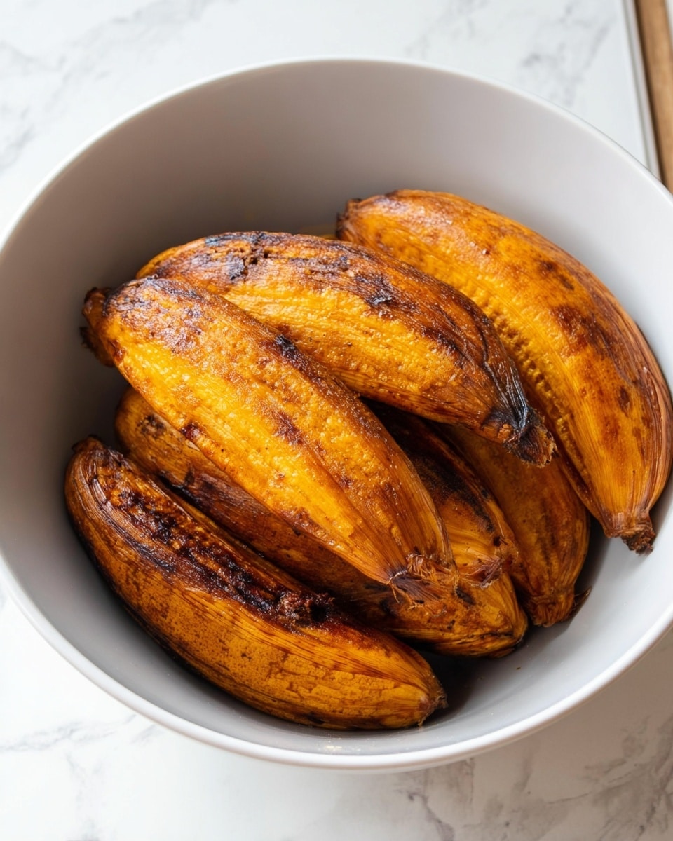 The image shows a white bowl filled with seven roasted plantains. Each plantain has a golden to dark brown color with a slightly wrinkled texture and some charred spots, showing they are cooked. The plantains are stacked closely together inside the bowl, with their shapes curved and elongated. The bowl is placed on a white marbled surface. photo taken with an iphone --ar 4:5 --v 7