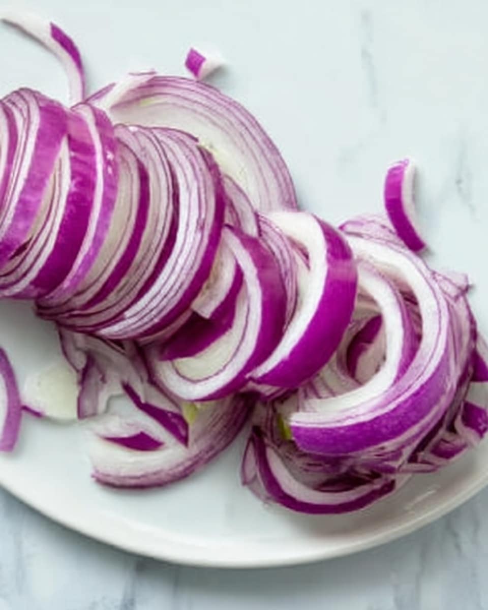 A close-up view of a white plate showing thinly sliced red onion pieces arranged loosely, forming a curved line across the plate. The onion slices have layers that show a mix of deep purple and white colors with a smooth, slightly shiny texture. Small pieces of onion are spread around the edges. The background is a white marbled surface with soft shadows from the onion slices. Photo taken with an iphone --ar 4:5 --v 7
