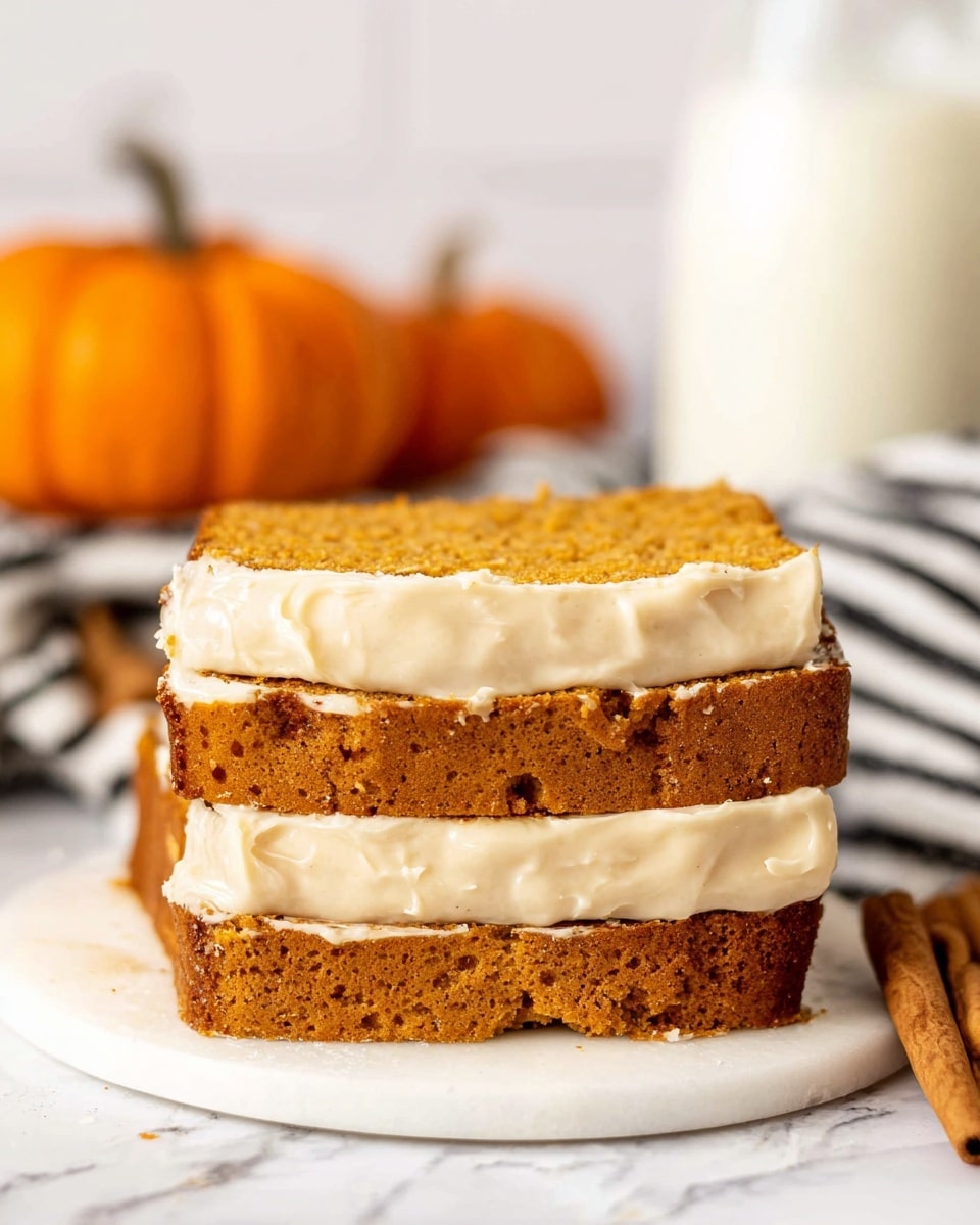 The image shows three thick slices of pumpkin bread stacked on top of each other on a white marbled surface. Each slice has a golden-brown crust and is covered with a thick layer of cream-colored frosting that looks smooth and creamy. In the background, there are two small orange pumpkins and a striped black and white cloth, slightly out of focus. To the side, a cinnamon stick lies on the surface, adding a warm, rustic touch. A glass of milk is also visible in the background, enhancing the cozy feel of the scene. photo taken with an iphone --ar 4:5 --v 7
