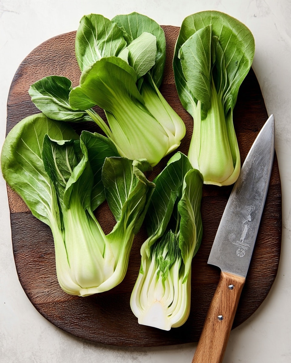 Several fresh green bok choy halves are arranged around a large silver knife with a wooden handle on a round brown cutting board. The bok choy layers show smooth white stems at the bottom, transitioning into vibrant green leaves with soft texture and veins at the top. The cutting board sits on a white marbled surface, adding contrast to the green and white colors of the bok choy and the silver knife. photo taken with an iphone --ar 4:5 --v 7