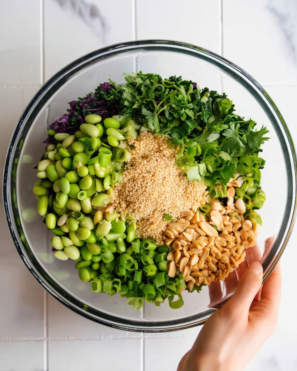 The image shows a clear glass bowl on a white marbled surface, filled with layers of fresh salad ingredients neatly arranged. At the bottom left, there are bright green edamame beans, next to chopped green onions on the lower right. Above the onions, there are crushed peanuts, and in the center, a pile of light tan sesame seeds. On the top right, there is fresh green cilantro, and next to it on the top left, chopped dark purple cabbage mixed with green kale. A woman's hand is holding the bowl from the side. The colors are fresh and vibrant, and the textures range from smooth beans to crunchy peanuts and leafy greens. Photo taken with an iphone --ar 4:5 --v 7