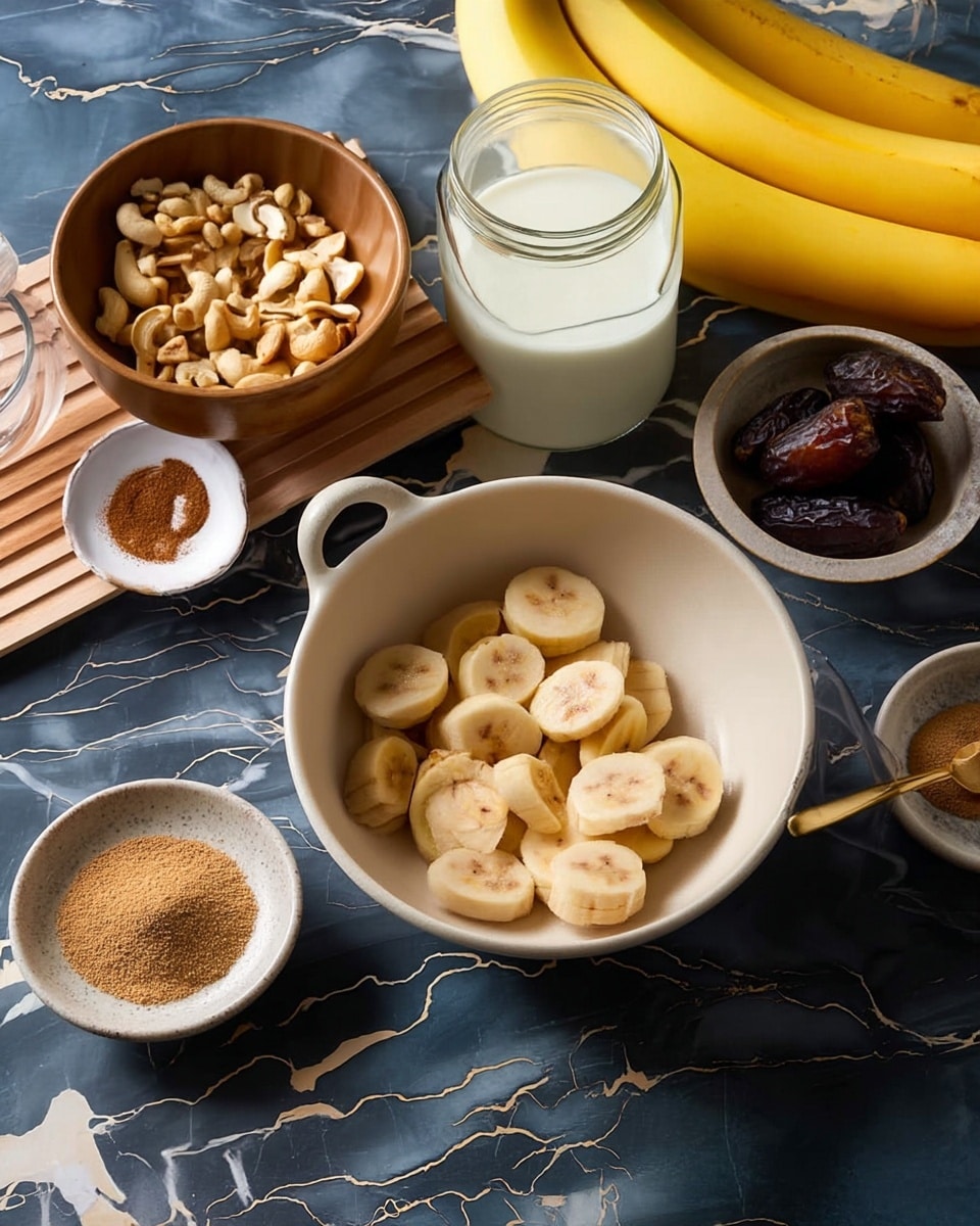 The image shows a round white bowl near the center filled with several slices of banana, stacked moderately, showing their creamy pale yellow inside and soft texture. Surrounding the bowl, there are smaller light gray bowls with dark brown dates, a small bowl with a dark brown powder and a golden small spoon, and a white dish with a round pile of light brown cinnamon powder. A wooden bowl on the left holds many whole cashews, resting on a rectangular wooden board. Nearby, an open glass jar filled with white milk sits on a dark blue marbled surface with white veins. At the right edge, there is a bunch of two whole bright yellow bananas with smooth peel. The scene is lit softly to show natural colors and textures. Photo taken with an iphone --ar 4:5 --v 7