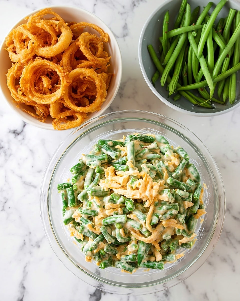 A clear glass bowl sits on a white marbled surface, filled with a thick creamy mixture of chopped green beans and shredded cheese, the green beans are bright green and the cheese is a soft yellow, giving the dish a textured and chunky look. Above the bowl, to the left, is a white bowl of golden crispy fried onion rings, and to the top right, a white bowl filled with fresh whole green beans. The whole setup looks fresh and ready to be mixed or served, photo taken with an iphone --ar 4:5 --v 7