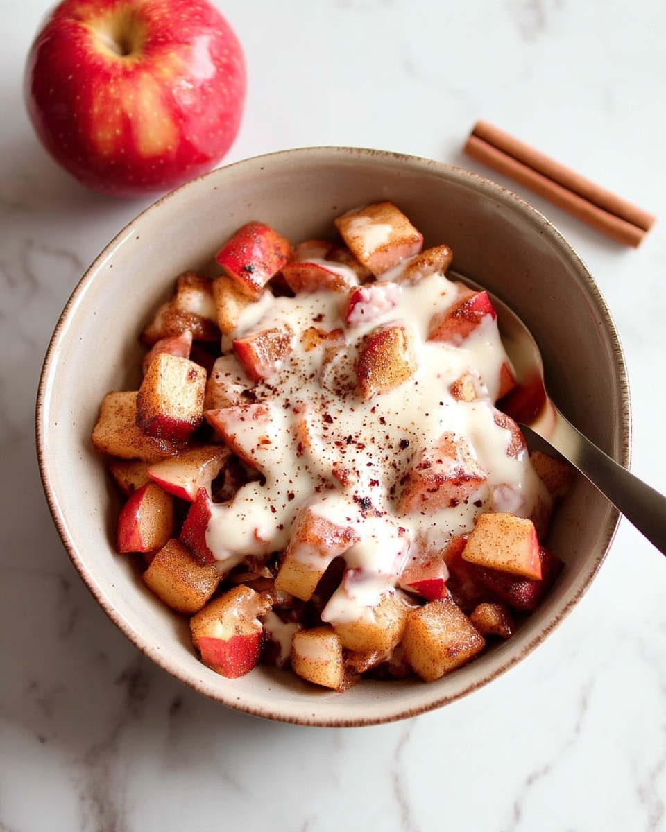 A light brown bowl filled with small, cooked pieces of red and light yellow apple with a soft texture, mixed and coated with cinnamon and sugar, creating a warm brown and reddish color tone throughout the fruit pieces. On top, there is a creamy white sauce or yogurt spread unevenly over the apples, slightly melting into the fruit below. A spoon rests inside the bowl on the right side, and the bowl is placed on a white marbled surface with a cinnamon stick and a red apple near it. Photo taken with an iphone --ar 4:5 --v 7