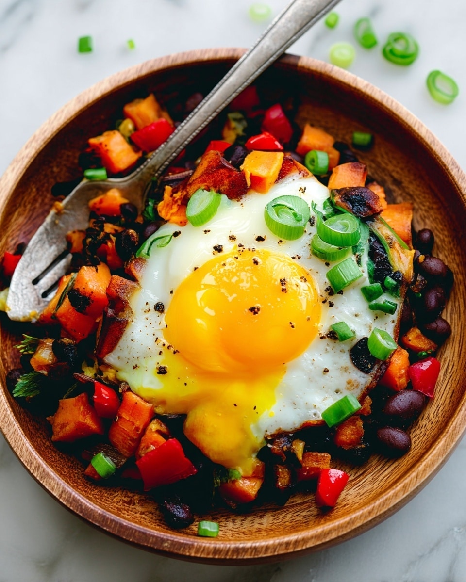 A wooden bowl holds a colorful dish with three main layers. The bottom layer consists of cooked diced sweet potatoes and black beans mixed with red bell pepper pieces, adding orange, black, and red colors with a slightly crispy texture. On top of this, there is a single fried egg with a white cooked edge and a bright yellow, runny yolk in the center, broken slightly to show the runniness. Chopped green onions are sprinkled over the egg and vegetables, adding green spots across the dish. A silver spoon rests inside the bowl, scooping up some of the food. The bowl is placed on a white marbled surface with some green onion pieces scattered around. Photo taken with an iphone --ar 4:5 --v 7