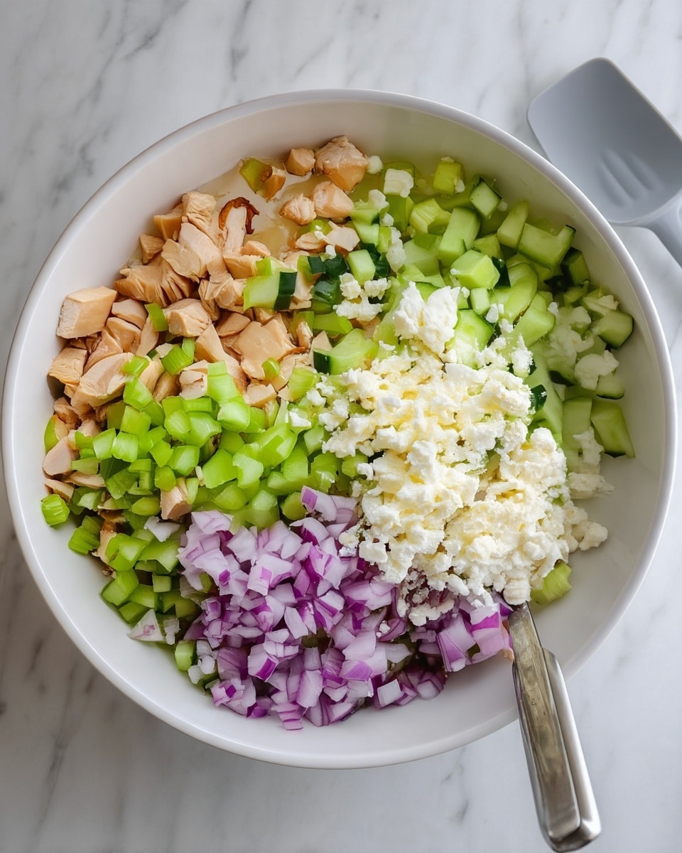 In a large white bowl, five distinct layers of food are arranged side by side. Starting from the top left, the first layer has small tan cubes of cooked chicken. Next to it is a layer of chopped celery with a bright green color. The middle layer is filled with finely diced cucumber, showing light and dark green colors. To the right of the cucumber is a white crumbly layer of cheese. The bottom layer consists of finely chopped red onions with their purple and white shades. The bowl is placed on a white marbled surface, and a gray spatula lies to the right side of the bowl. photo taken with an iphone --ar 4:5 --v 7