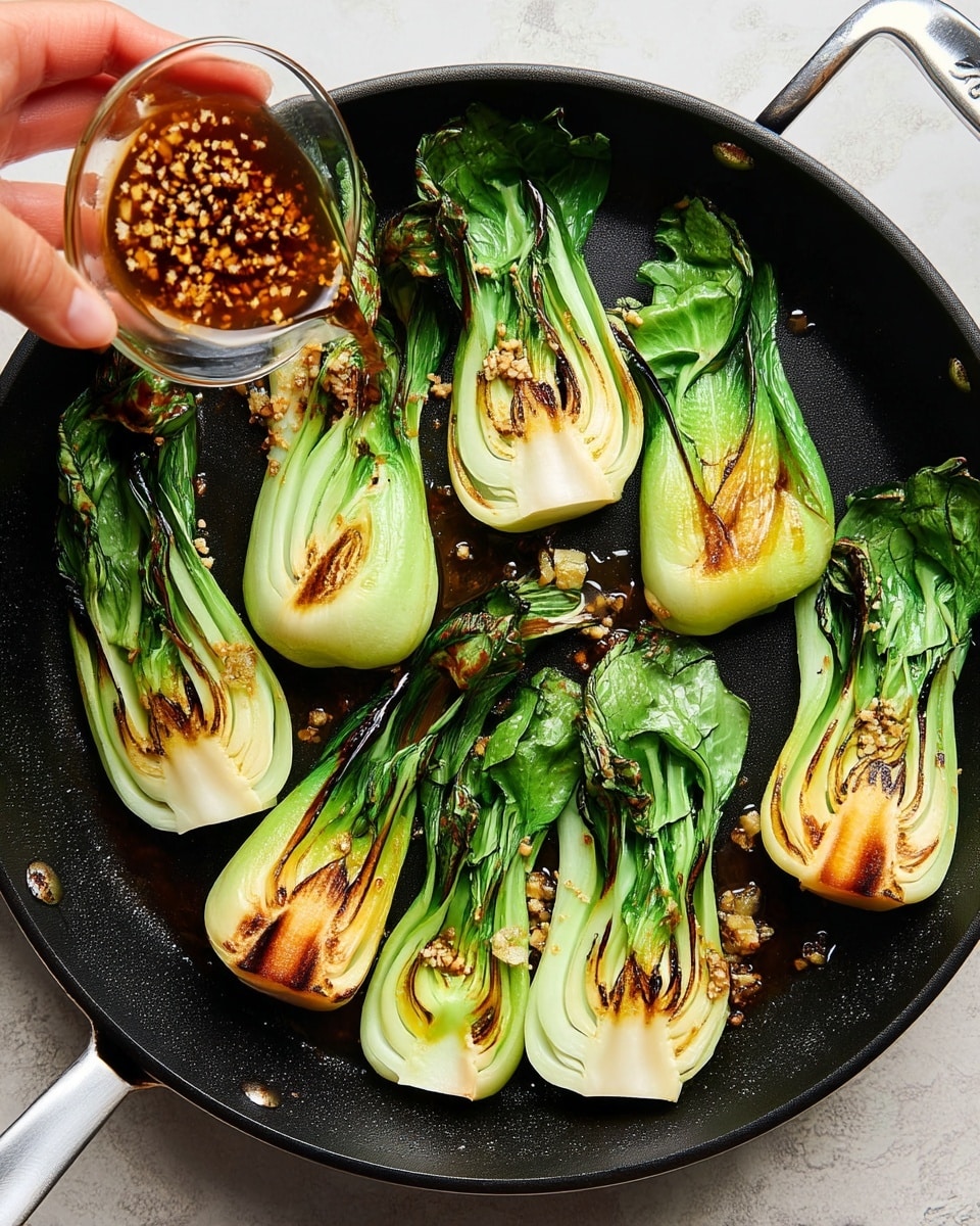 A black pan holds eight pieces of bok choy, each cut in half lengthwise, placed flat with the cut side up. The bok choy layers show a pale green to white center with bright green leafy edges, all with toasted brown grill marks. On top of the bok choy, there are small bits of minced garlic scattered. A woman's hand is seen pouring a brown sauce with minced garlic from a small clear glass bowl onto the bok choy. The pan rests on a white marbled surface. photo taken with an iphone --ar 4:5 --v 7