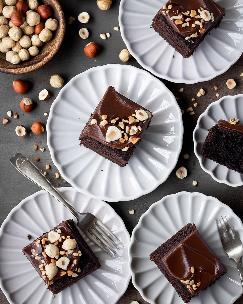 The image shows several square pieces of chocolate cake on white, scalloped-edge plates. Each piece has two layers: a dark, moist chocolate base and a smooth, thick layer of glossy chocolate frosting on top. The frosting is decorated with whole and chopped hazelnuts scattered over one side of the cake. Some plates also have vintage silver forks placed beside or touching the cake. Around the plates, there are loose hazelnuts and crumbs spread over a dark gray surface. In the upper left corner, a rustic wooden bowl holds more hazelnuts. The simple presentation contrasts dark chocolate tones with the light white plates and scattered nuts. Photo taken with an iphone --ar 4:5 --v 7