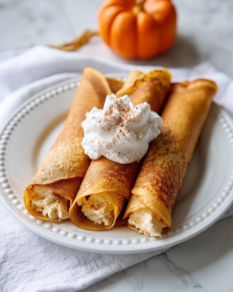 Three rolled crepes filled with a light tan cream are placed side by side on a white plate with a simple dotted edge. On top of the middle crepe is a dollop of white whipped cream sprinkled with brown cinnamon powder. The plate sits on a white cloth with a small orange pumpkin in the blurred background, all on a white marbled surface. The crepes have a golden brown color with a slightly crispy texture on the outside. photo taken with an iphone --ar 4:5 --v 7